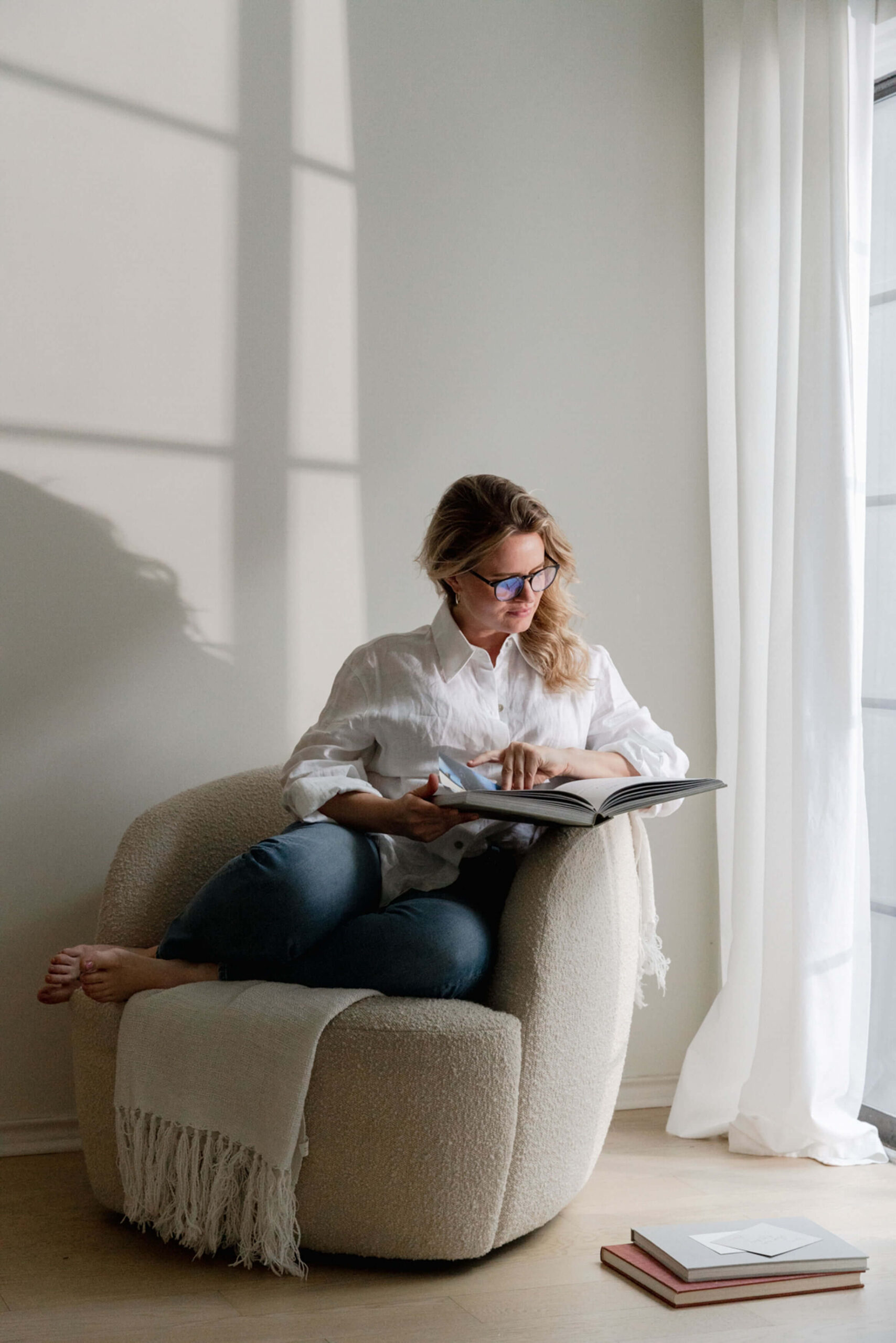 How to stop overthinking decisions. A woman sitting in a cosy chair by a sunlit window in a quiet moment of reflection.