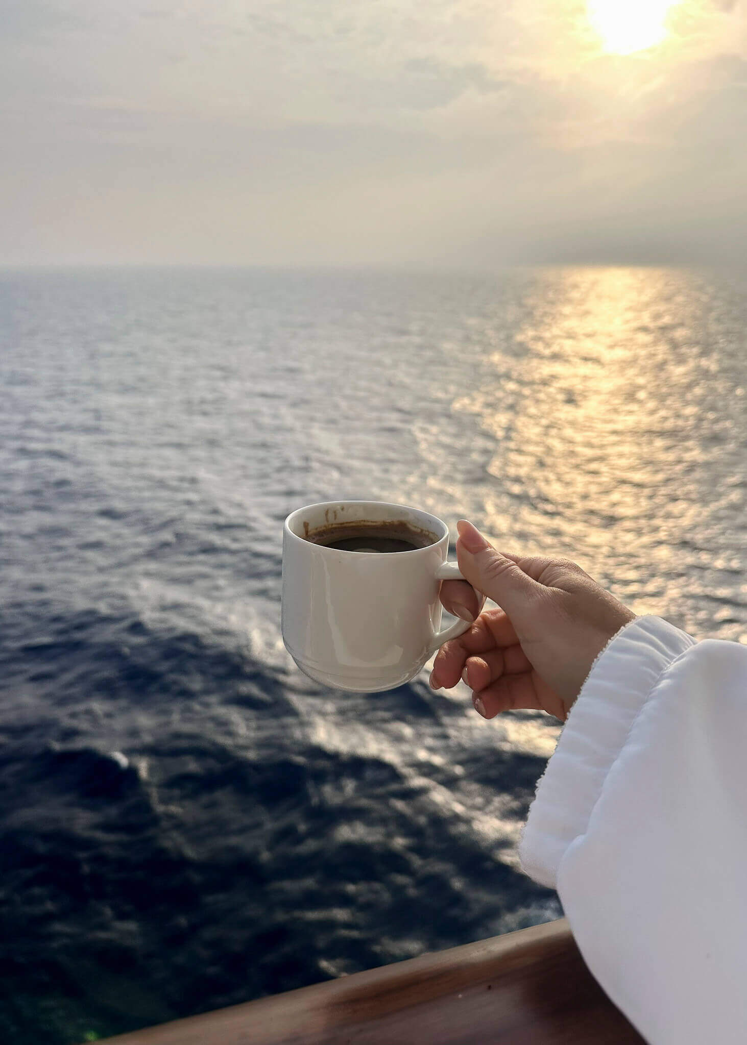 Woman holding a coffee cup at sunrise, taking a quiet morning moment to slow down from wellness fatigue in midlife.